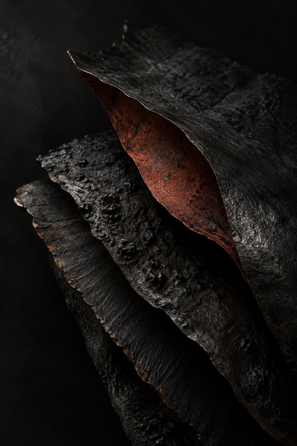 Layered charcoal plates lifting to expose an oxide-red underside